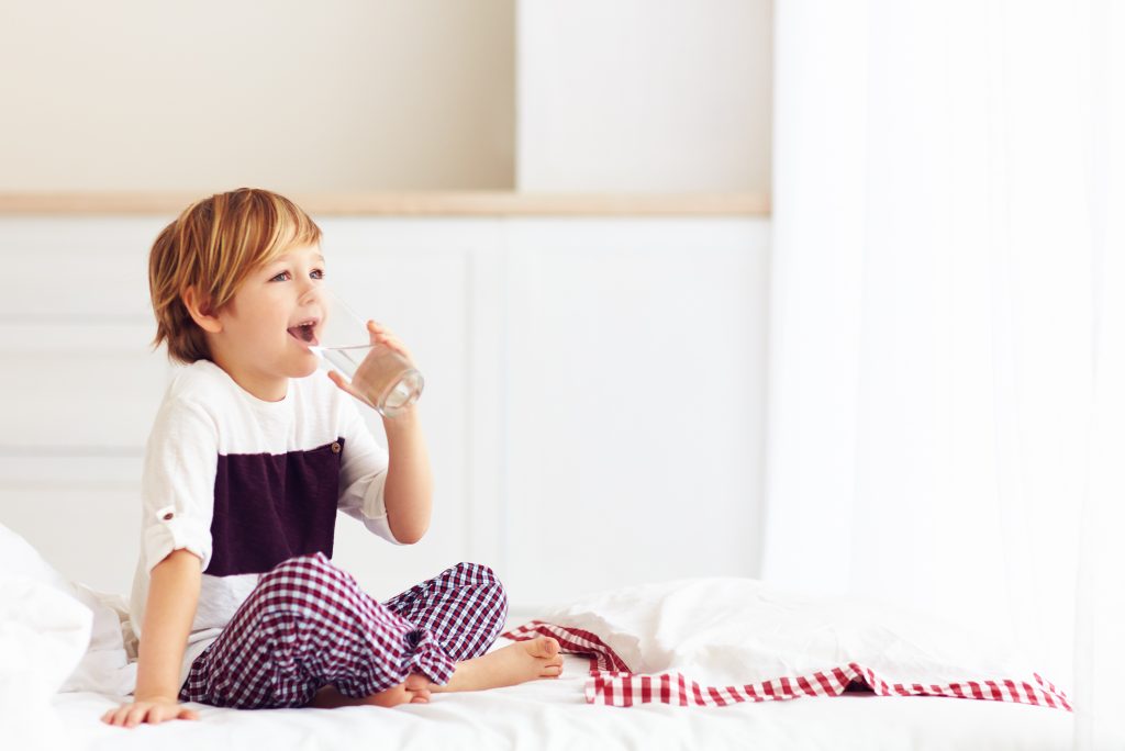 young boy drinks a glass of water whist sitting in bed